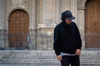 a man in a black hoodie standing in front of a building