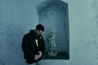 a man in a black jacket standing next to a statue